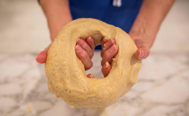 4) Dar forma. Untarse las manos en aceite. Dividir la masa en tres porciones, formar bolas, hundir el dedo hasta abrir un agujero en el centro de una de las bolas y, sosteniéndola en el aire, girarla para que se estire por su propio peso. Una vez formado cada roscón, ponerlo en una placa de horno con un papel de hornear debajo, cubrir con otro papel de horno engrasado con aceite para que no se pegue. Dejar reposar en sitio fresco toda una noche.