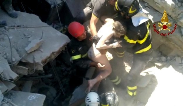 Los bomberos rescatan a Ciro, un niño de once años, sepultado entre los escombros de su casa. A la izquierda, equipos de rescate buscan supervivientes entre los restos de edificios destruidos por el seísmo el lunes por la noche. :: efe