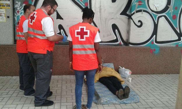Personal de Cruz Roja durante una intervención con una persona que duerme en plena calle sobre un colchón rescatado de la basura. /SUR