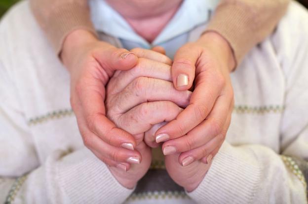 Un cuidador coge las manos de un anciano con una demencia. :: r. c./