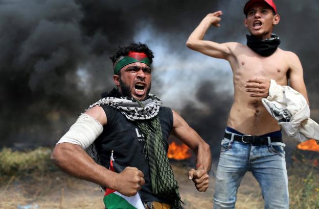 Dos palestinos se plantan ante los soldados israelíes durante las protetas en la frontera de Gaza. / I. A. M. / REUTERS