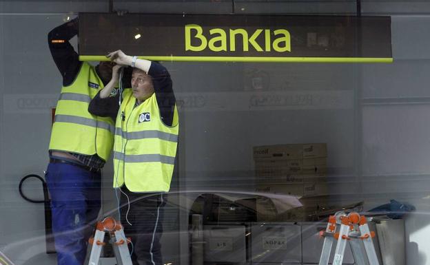 Dos trabajadores colocan un cartel de Bankia en una oficina de Madrid. /Rocío Peláez (Reuters)